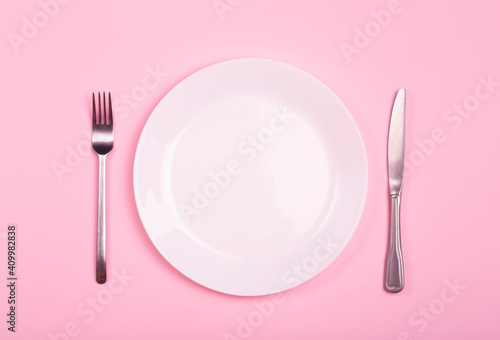 Empty plate on a pink background. White plate with knife and fork on a pink empty table