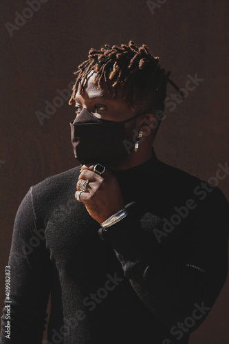 African American male in black outfit and protective mask standing on street and looking away during COVID 19 epidemic
