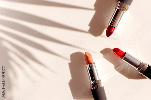 Fashion colorful lipsticks sun shadows from palm leaf on beige background flat lay top view. Beauty and cosmetics background. Decorative cosmetics makeup women's lipstick beauty brand product design photo
