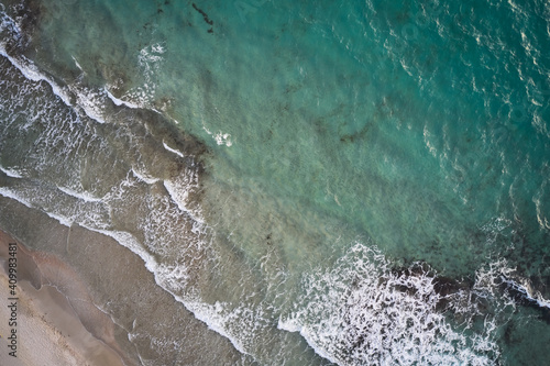 Aerial top view of turquoise water with seaweed and foamy waves rolling on empty sandy beach photo