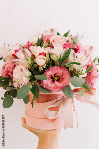 Fototapeta Naklejka Na Ścianę i Meble -  Bouquet with pink anemones and roses and eucalyptus branches in round pink box. In hand. Satin ribbon on the box. Present, spring time, happy women's day