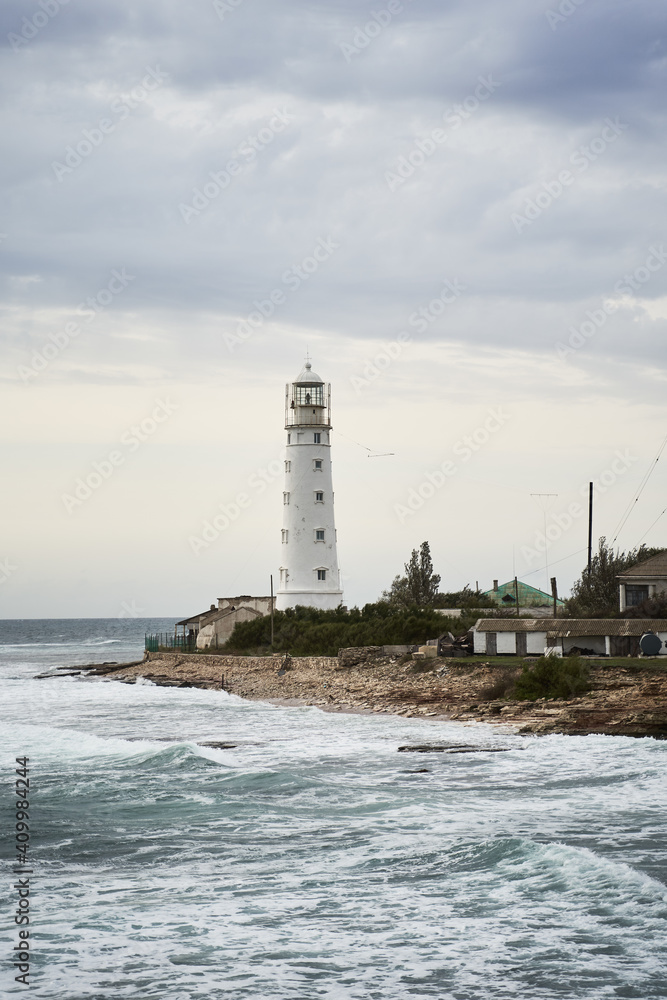 Tower of white beacon located on coast near waving sea under overcast sky Tower of white beacon located on coast near waving sea under overcast sky