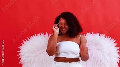 african latin cupid woman in wtite top bra holding bow and arrow in red studio The 14th of February Valentine's Day photo