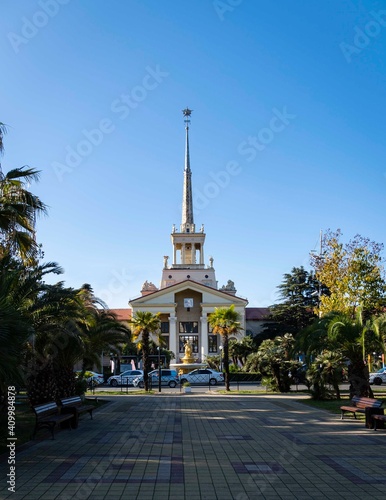 Sochi, Russia - December 07, 2020: Building of sea trade port with spire from side of city landscape park. In front of building there is fountain with sculptural composition. Place to rest