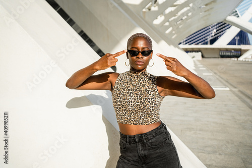 African American female with short hair in cool sunglasses standing on street showing fuck gesture while looking at camera