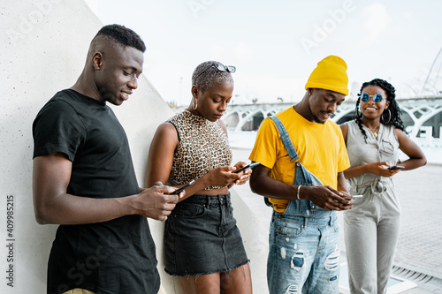 Young black people in stylish clothes standing in urban area and messaging on social media via smartphones photo