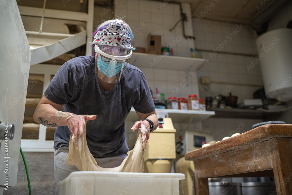 Unrecognizable female baker in mask working in bakery and kneading raw dough while cooking delicious bread Unrecognizable female baker in mask working in bakery and kneading raw dough while cooking delicious bread