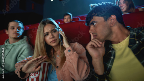 Portrait of attractive young woman talking on the phone, annoying her boyfriend while having romantic movie date at the cinema