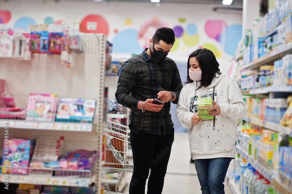 Asian couple wear in protective face mask shopping together in supermarket during pandemic. Online buying on smartphone is better choice.
