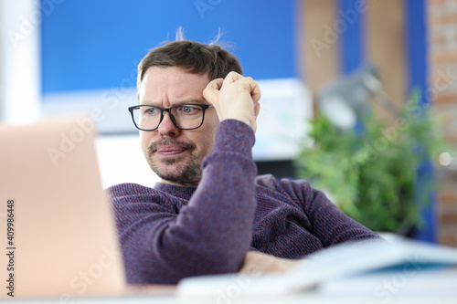 Fotografie Disgruntled man with glasses looking at laptop screen