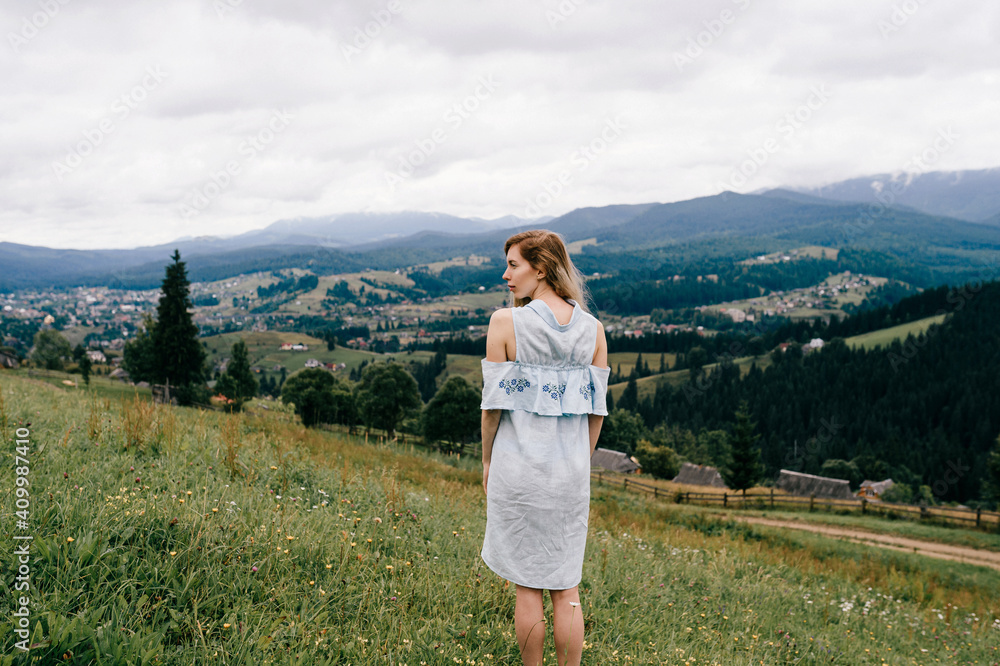 Young attractive elegant blonde girl in blue romantic dress posing back over picturesque landscape