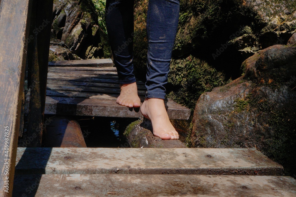 Feet of woman walking without shoes on small wooden bridge in the river Feet of woman walking without shoes on small wooden bridge in the river