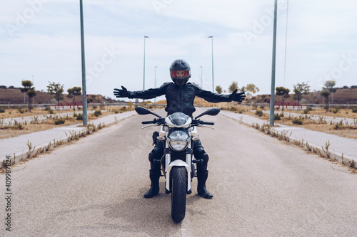 Full body of unrecognizable motorcyclist in black outfit and helmet sitting on modern motorbike parked on roadway