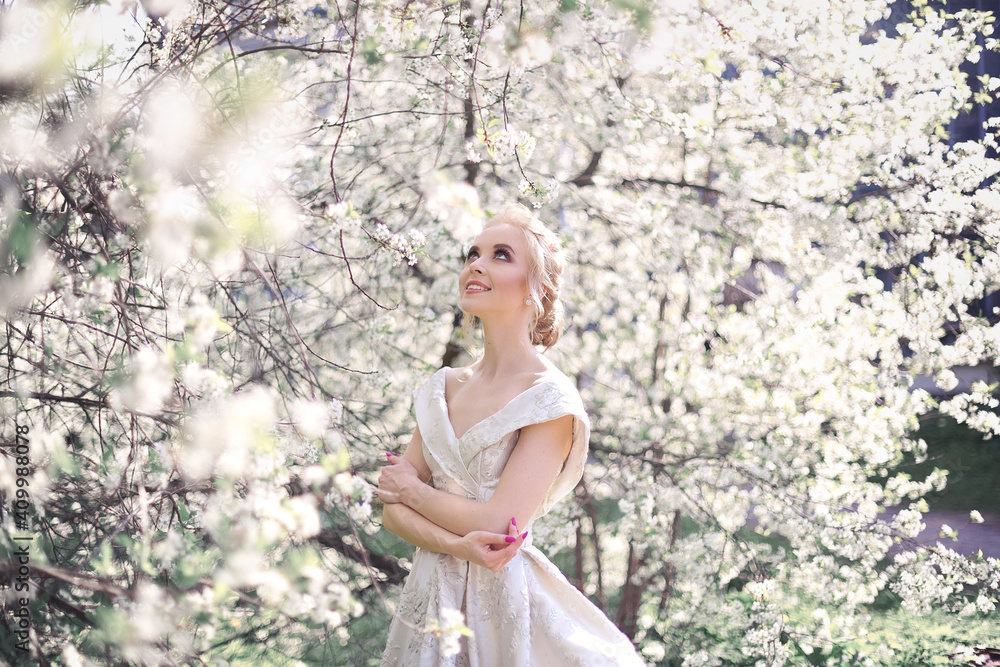 A beautiful blonde girl in a luxurious white brocade haute couture dress with a long train and open shoulders walking in a blooming orchard A beautiful blonde girl in a luxurious white brocade haute couture dress with a long train and open shoulders walking in a blooming orchard