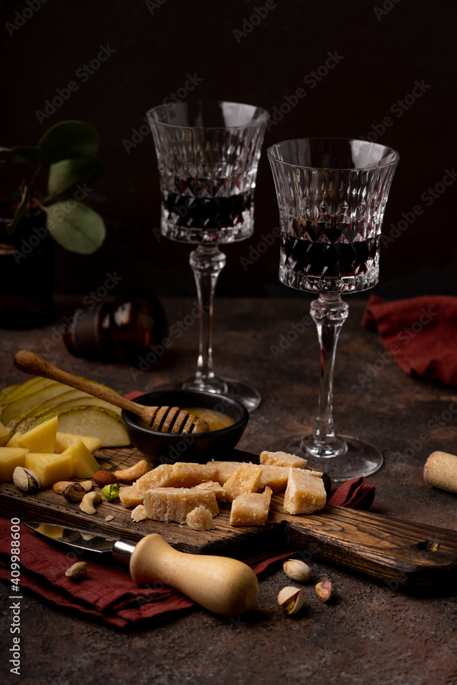 Cheese platter with different cheeses, sliced pear, nuts, honey and glasses of red wine on rustic wooden background. Retro styled cheese variety selection on wood board. Selective focus.