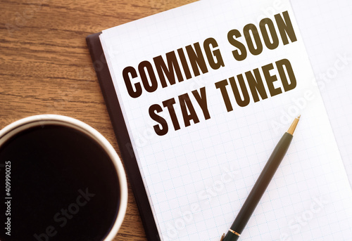 COMING SOON STAY TUNED. Text on notepad on wooden desk.