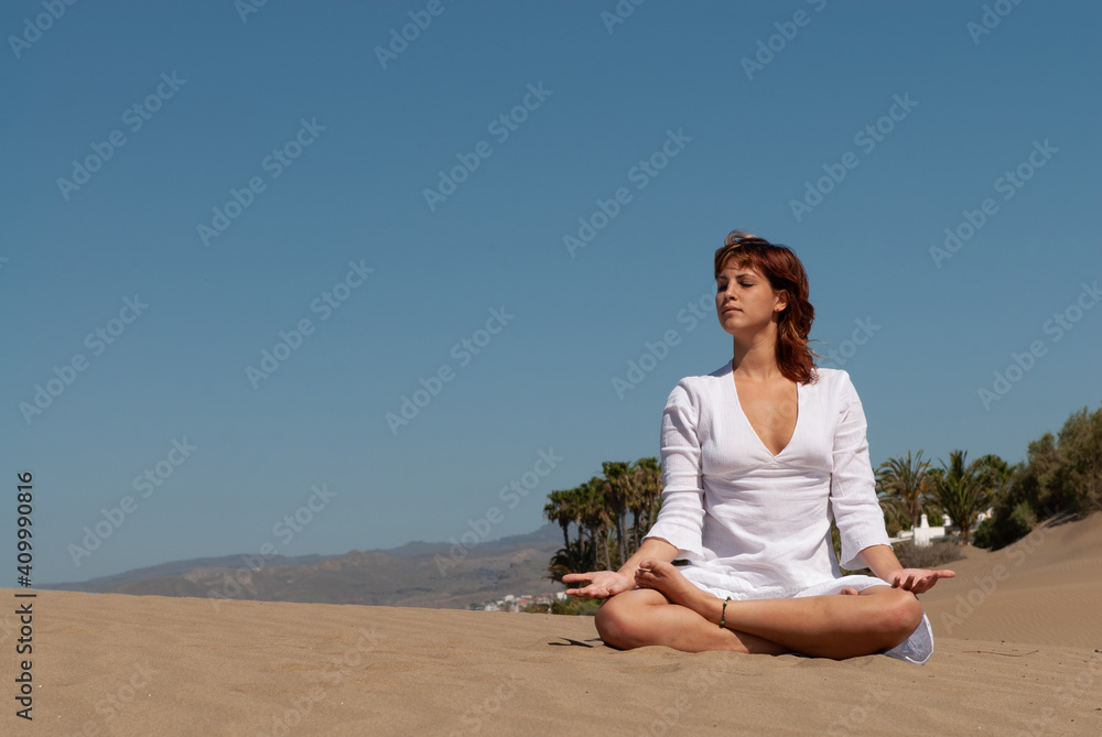 woman dressed in white performing meditation and yoga postures on the sand dunes on sunny day woman dressed in white performing meditation and yoga postures on the sand dunes on sunny day