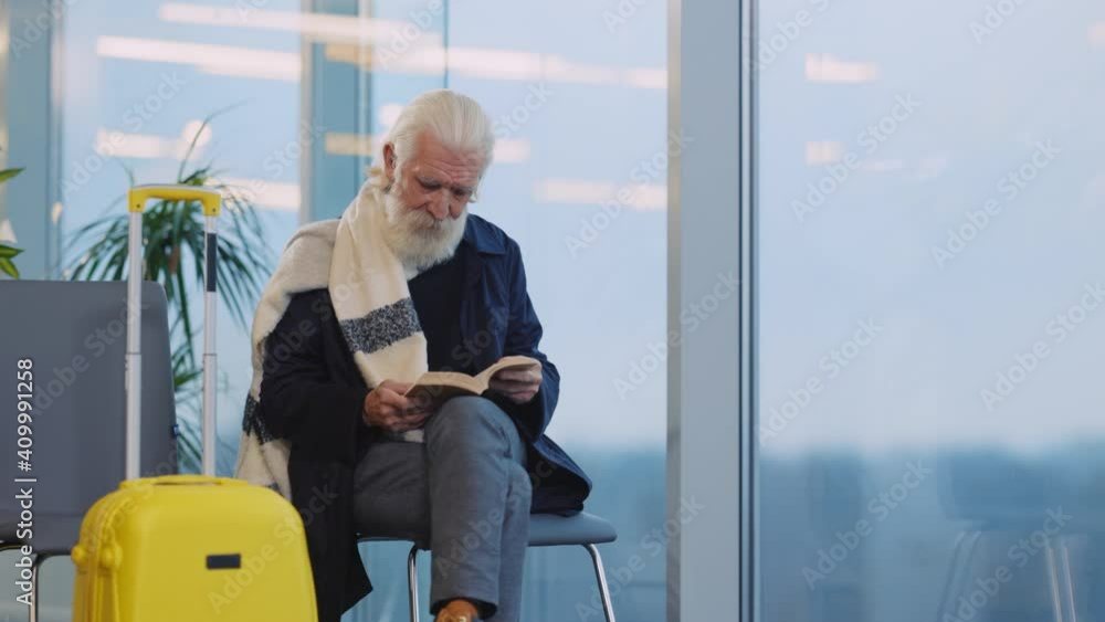 Old Handsome Intelligent Man in Stylish Clothes Waiting in Airport Reading Storybook Spending Time. Departure Lounge. Terminal Interior. Business People. Old Handsome Intelligent Man in Stylish Clothes Waiting in Airport Reading Storybook Spending Time. Departure Lounge. Terminal Interior. Business People.