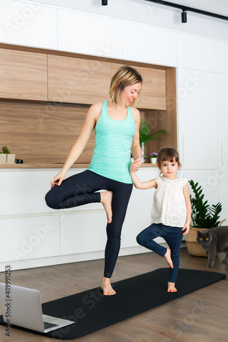 Woman and her little daughter are standing in a Tree Pose