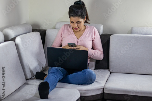 Young woman typing on her cell phone in front of her laptop at home
