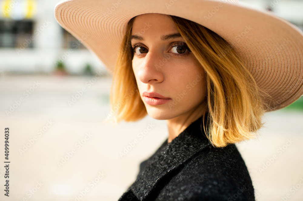 Close up portrait of elegant stylish blonde short hair girl in hat posing over street background