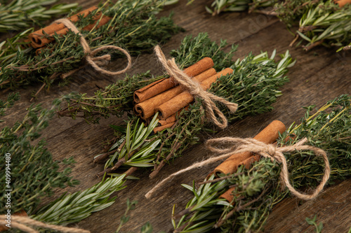 bundles with herbs and cinnamon sticks tied together with a bow on wooden table 