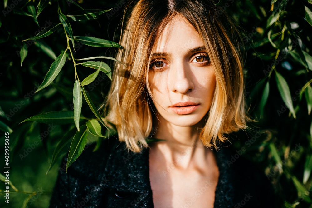 Portrait of elegant stylish blonde short hair girl posing in the park over green branches Portrait of elegant stylish blonde short hair girl posing in the park over green branches