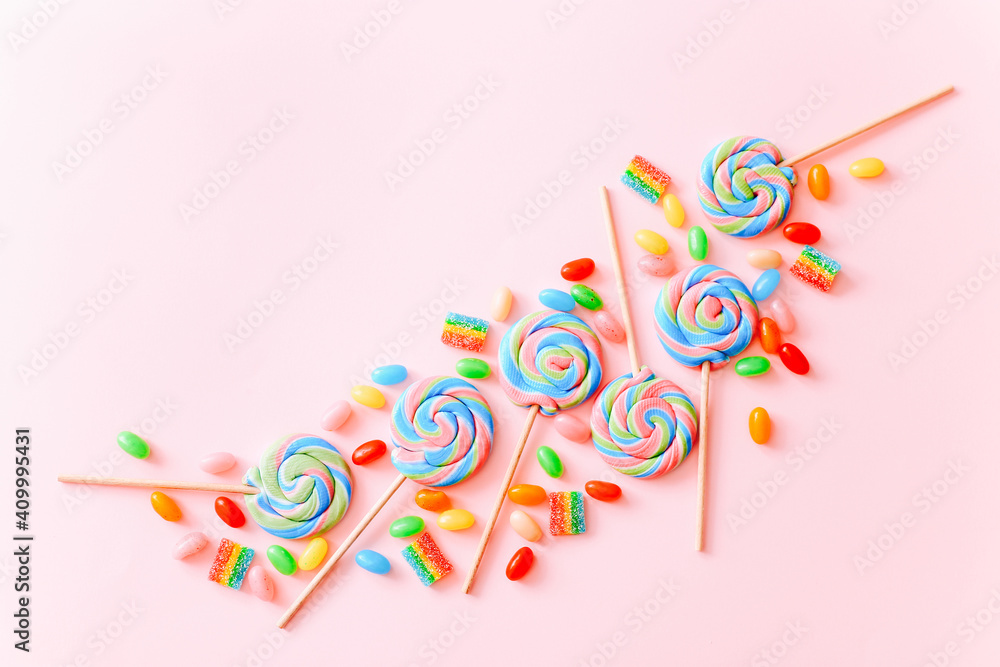 Fototapeta premium Colorful lollipops swirls on sticks. Striped spiral multicolored candy on pink background, top view