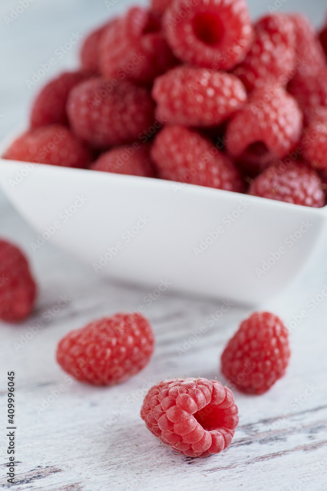 Ripe raspberry in small white bowl on white a wooden background. Ripe raspberry in small white bowl on white a wooden background.