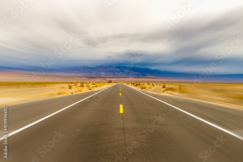 Rural California desert road with motion blur and background of mountains and clouds.