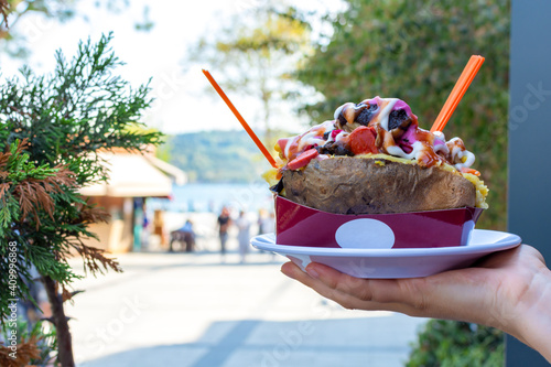 Photography Photo of baked potato (turkish: kumpir) stuffed with the cheese, sausage, olives, peppers, corn, ketchup, mayonnaise