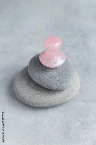 Pink Gua Sha facial massage and face care tool. Rose Quartz gua sha mashroom shape stone on grey stone pyramid on concrete background. Anti age, face yoga, lifting and toning treatment at home. Copy