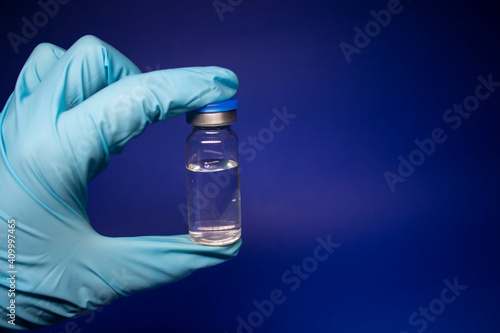 Development of coronavirus vaccine COVID-19. bottle phial with no label in blue medical glove. isolated on blue background. cure. Vaccination for prevention and treatment to infections