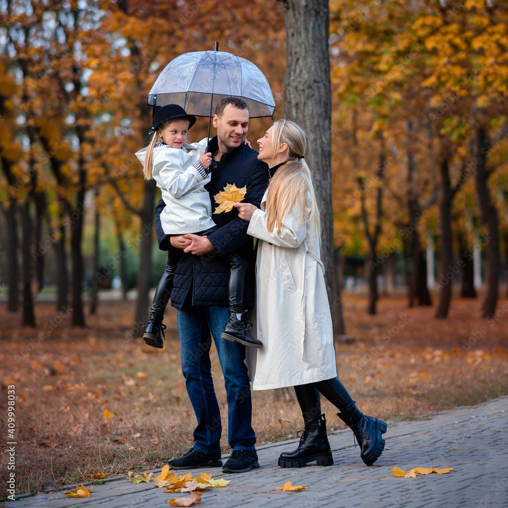 Fototapeta premium Happy family on a walk in the park under an umbrella