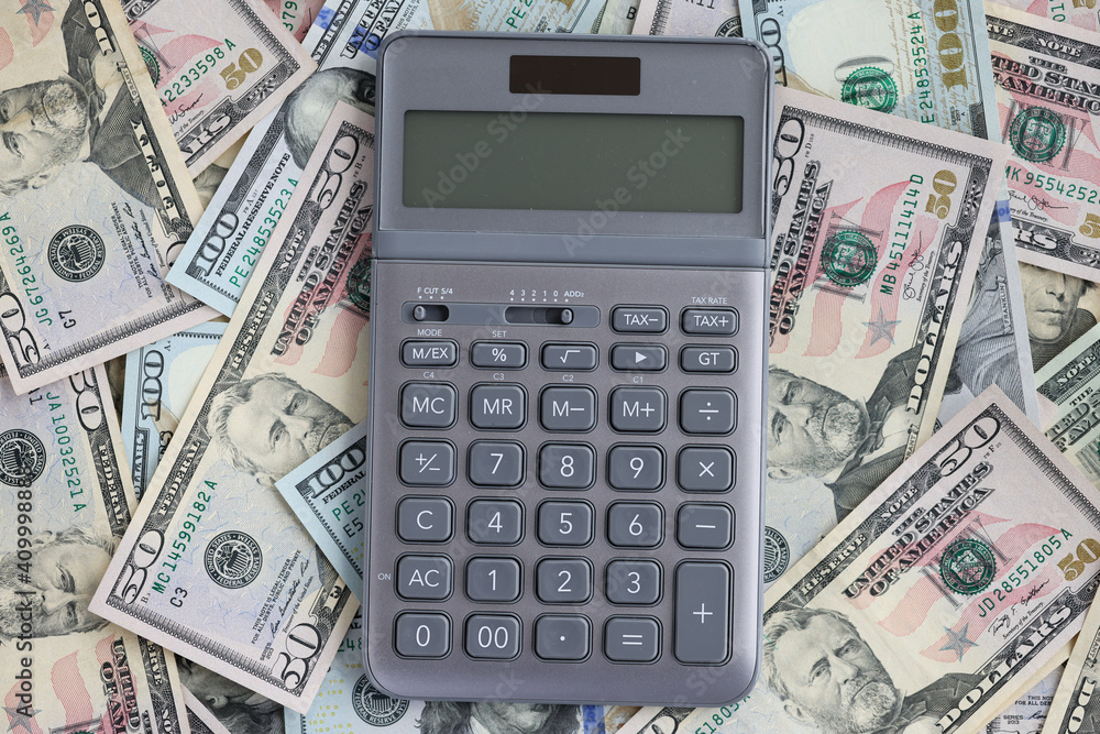Calculator lying on set of American dollar bills closeup Calculator lying on set of American dollar bills closeup