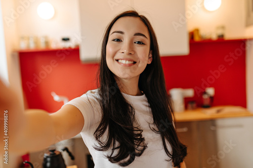 Woman in great mood takes selfie in kitchen. Portrait of brown-eyed girl photo