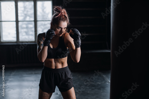 cool female fighter in boxing gloves trains in the gym. Mixed martial arts