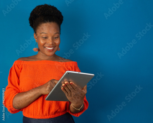 black woman smiling and holding a tablet ih her hands on studio with a blue background