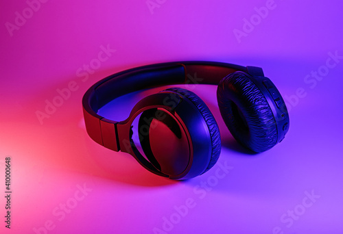 Stylish black wireless headphones lit with colorful neon light on abstract background isolated. Modern technology concept with copy space