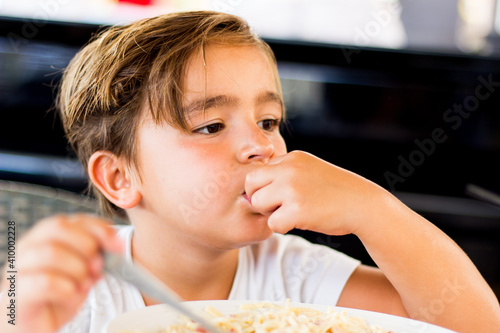 child pensively at the table eating pasta