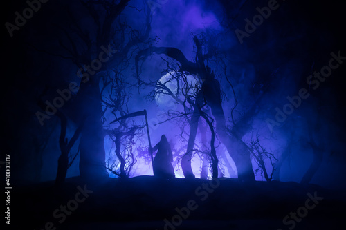Death with a scythe in the dark misty forest. Woman horror ghost holding reaper in forest, halloween concept © zef art