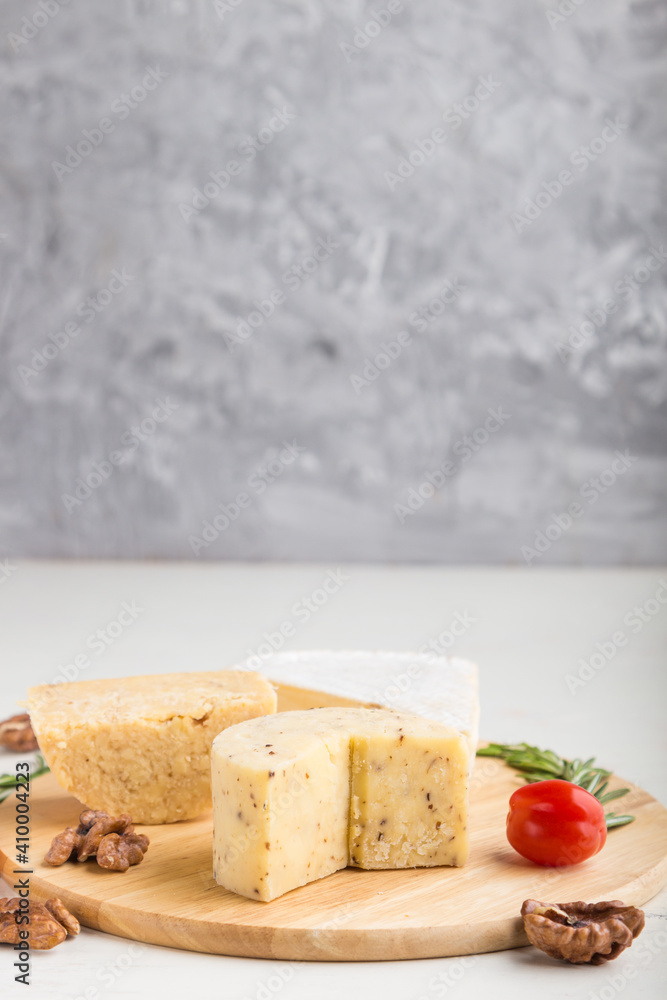 Cheddar and various types of cheese with rosemary and tomatoes on wooden board on a gray and white background . Side view, copy space.