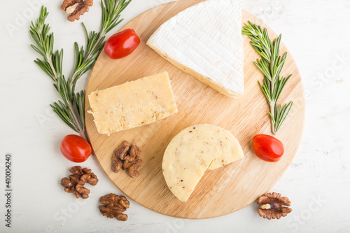 Cheddar and various types of cheese with rosemary and tomatoes on wooden board on a white background . Top view.