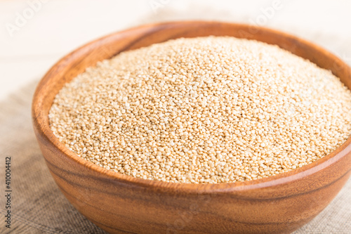 Wooden bowl with raw white quinoa seeds on a white wooden background. Side view, selective focus.