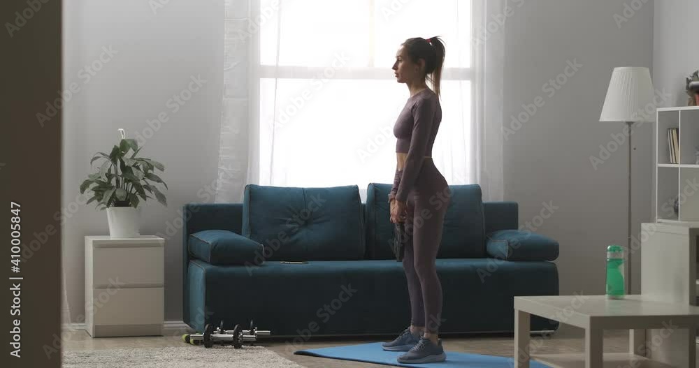 sporty woman dressed sportswear is doing squats with weight in hands, training body, keeping fit, full-length shot in apartment sporty woman dressed sportswear is doing squats with weight in hands, training body, keeping fit, full-length shot in apartment