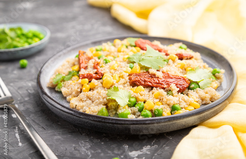 Quinoa porridge with green pea, corn and dried tomatoes on ceramic plate on a gray concrete background. Side view, selective focus.