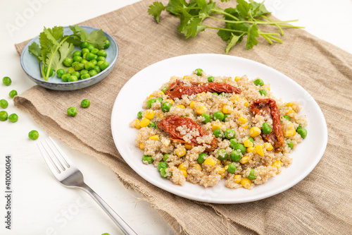 Quinoa porridge with green pea, corn and dried tomatoes on ceramic plate on a white wooden background. Side view.