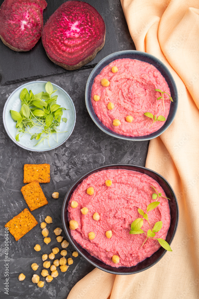 Hummus with beet and microgreen basil sprouts in wooden bowl on a black concrete background. Top view, close up. Hummus with beet and microgreen basil sprouts in wooden bowl on a black concrete background. Top view, close up.