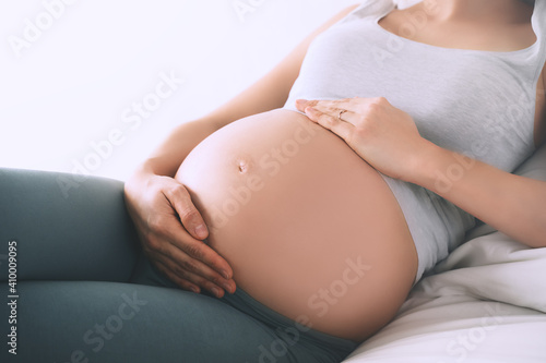 Beautiful relaxed pregnant woman holds hands on her belly in bedroom at home. Concept of wellbeing during pregnancy, maternity, healthcare, gynecology.