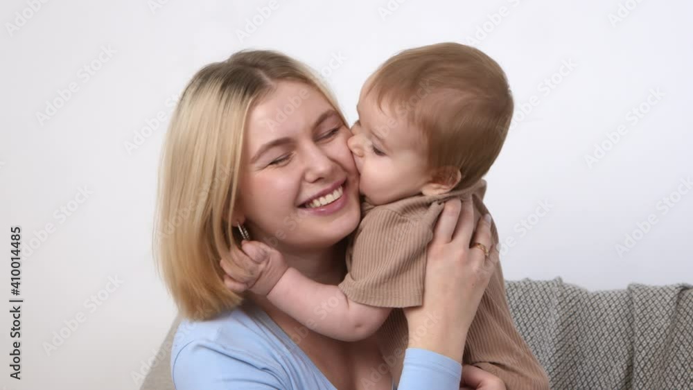 Young mother playing with her infant, baby kissing mom's cheek, spending time together, slow motion